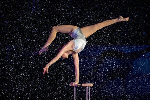 A person in a white leotard bends acrobatically, supporting themselves with one arm.