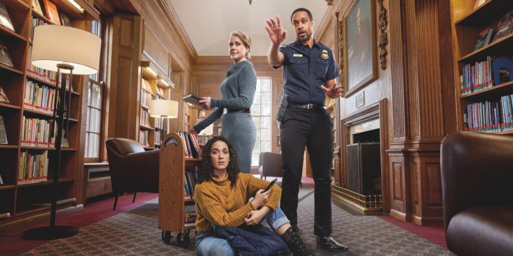 A scene from inside a library. The walls are made of wooden bookshelves and has an academic feel. Three people are at the center of the image: A librarian wearing a gray sweater dress, a police officer, and someone wearing a yellow sweater and black boots who sits on the floor.